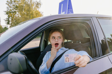 Young woman in eyeglasses with surprise emotion holds driving license. Driving school. Young...
