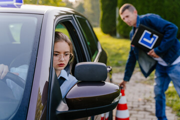 Naklejka premium Driving Test. Training parking. Cones for the examination, driving school concept. Alert nervous young teen girl student driver taking driving education lesson test from male instructor.