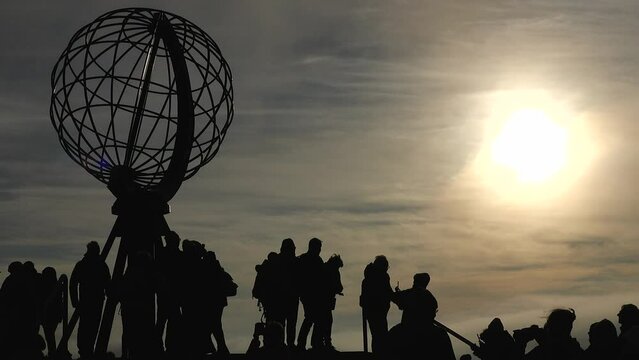 Nordkapp at Sunset with Colorful Clouds and Silhouette of Globe Monument and people. Globe monument at North Cape at midnight, island of Mageroya, Norway