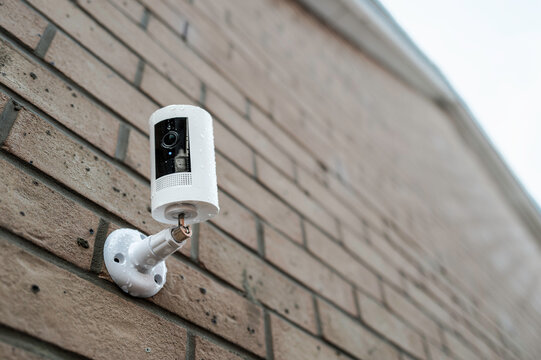 Shallow focus of a wireless smart CCTV night and day camera seen after a heavy downpour on a house exterior wall. The blue motion LED indicator is seen active, showing its recording.