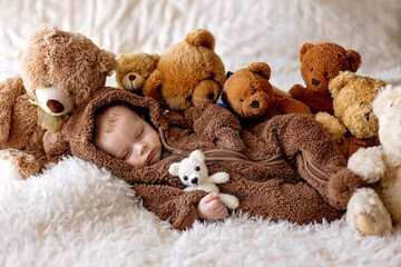 Sweet baby boy in bear overall, sleeping in bed with teddy bear.