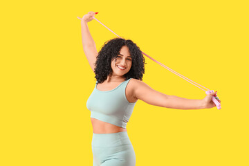 Sporty adult woman with skipping rope on yellow background