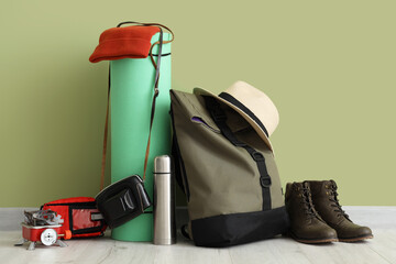 Set of camping equipment with backpack, portable stove, thermos and boots near green wall