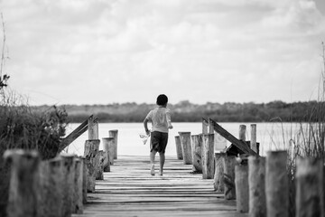 A boy running on a wooden bridge over a lake, black and white.