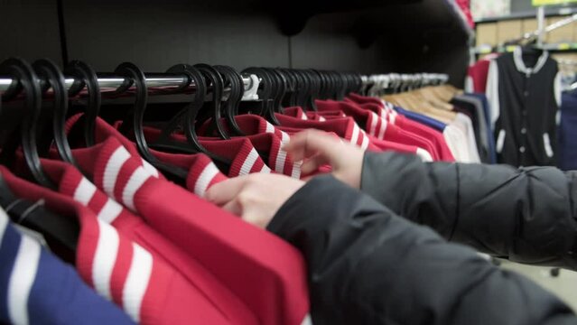 Shopper shopping in clothing store buys jacket choosing size on showcase hanger.
