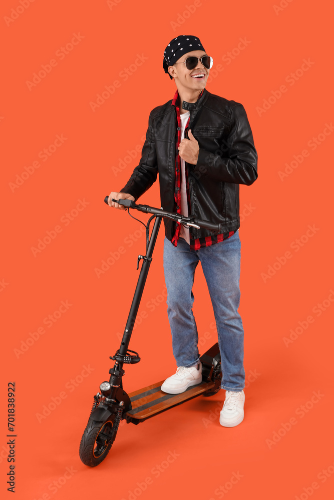 Poster Cool young man with kick scooter on orange background