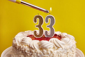 A candle in the form of the number 33, stuck in a holiday cake, is lit. Celebrating a birthday or a...