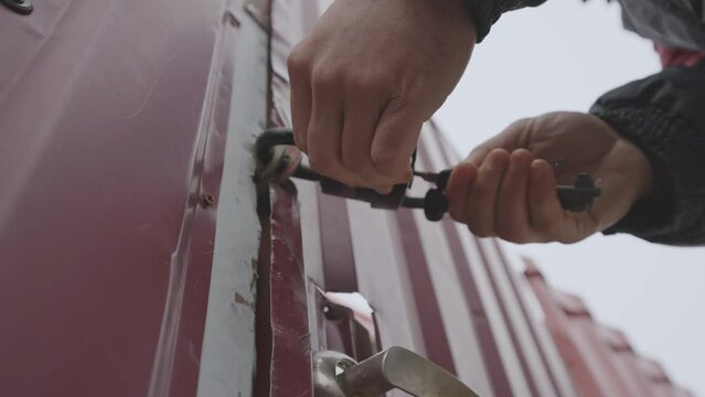 Hands of man with bunch of keys open padlock hanging on old metal door of warehouse or country home outside