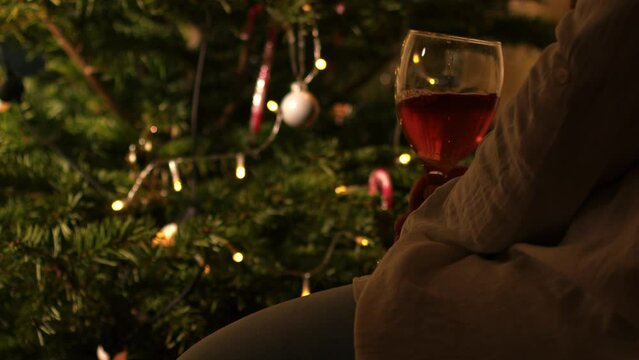 Woman relaxing with glass of red wine in front of Christmas tree