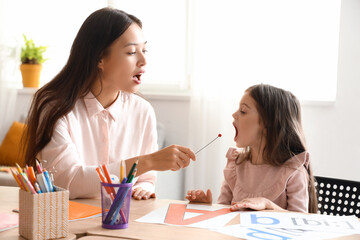 Female Asian speech therapist with logopedic probe and little girl in office