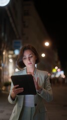 Vertical view of the beautiful young woman using tablet computer while walking through night city