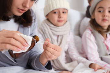 Mother pouring cough syrup for her ill daughter in bedroom, closeup
