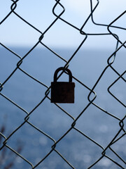 Vorhängeschloss am Zaun mit Blick auf das Meer – Symbol für Sehnsucht und Grenzen
