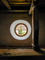 Beautiful round window overlooking a garden, window with glass frames in an old wall with old wooden beams at the Fortified church Biserica Evanghelica Fortificata Viscri, Deutsch-Weisskirch