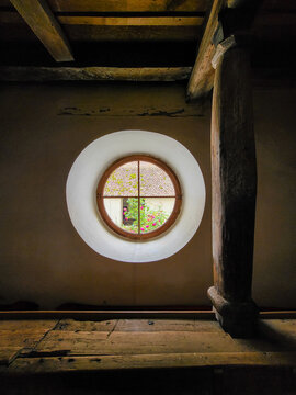 Beautiful round window overlooking a garden, window with glass frames in an old wall with old wooden beams at the Fortified church Biserica Evanghelica Fortificata Viscri, Deutsch-Weisskirch