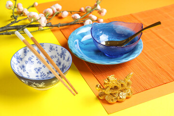 Bamboo mat with bowls, chopsticks and sakura branch on yellow background. Chinese table setting