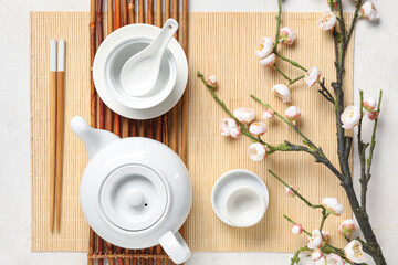 Teapot with dishes, chopsticks and sakura branch on white background. Chinese table setting
