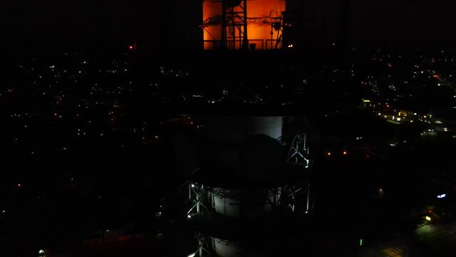 Aerial shot drone orbits to left in close up of observation tower at night