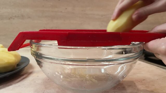 Slow motion 4k video grating potato on plastic shredder. Hands cookinghash browns close-up. Process of preparing flapjacks. Film grain pixel texture. Soft focus. Blur. Live camera