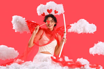 Young African-American woman dressed as Cupid with bow in clouds on red background. Valentine's Day...