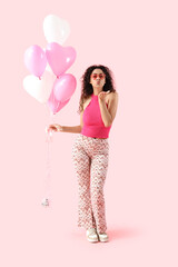 Young African-American woman with balloons blowing kiss on pink background. Valentine's Day celebration