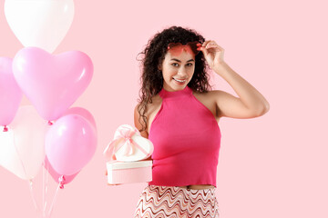 Young African-American woman with gift and balloons on pink background. Valentine's Day celebration