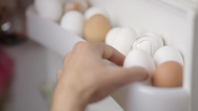 Hand takes white egg from fridge . Chicken eggs in box fridge	