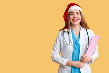 Young female doctor in Santa hat on yellow background