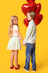 Little children with balloons holding hands on yellow background, back view. Valentine's Day celebration