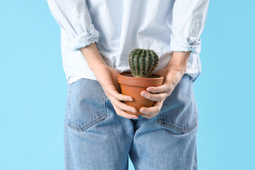 Young man with hemorrhoids and cactus on blue background, back view