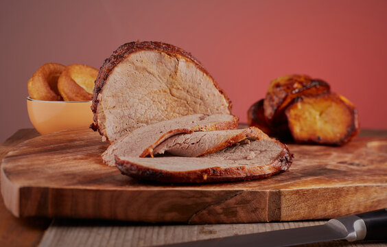 Beef  roast joint that has been sliced,with some yorkshire puddings and roast potatoes in the background.