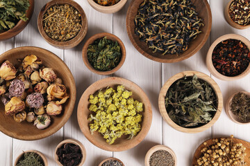 Many different dry herbs and flowers in bowls on white wooden table, flat lay