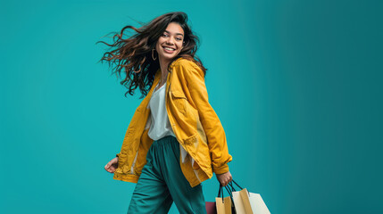 Stylish woman in a yellow coat walking and carrying shopping bags, against a solid teal background. - Powered by Adobe