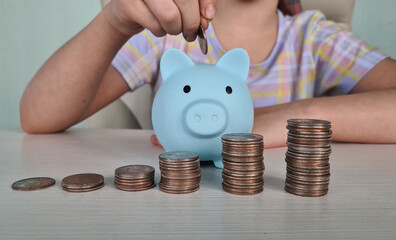 Child throws coin into toy blue piggy bank