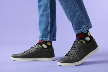 Man in stylish colorful socks, sneakers and jeans on violet background, closeup