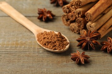 Spoon with cinnamon powder, sticks and star anise on wooden table, closeup