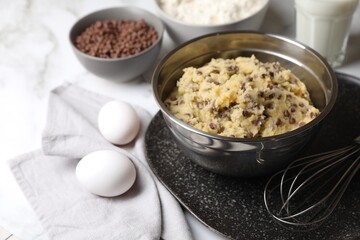 Chocolate chip cookie dough in bowl and ingredients on white wooden table, closeup
