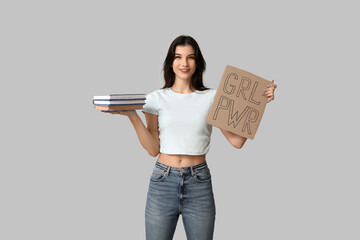 Young woman holding cardboard with text GRL PWR and books on grey background. Feminism concept