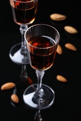 Liqueur glass with tasty amaretto and almonds on black table, closeup