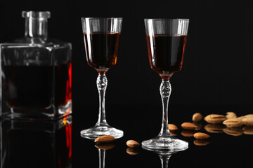 Liqueur glasses with tasty amaretto, bottle and almonds on black table, closeup