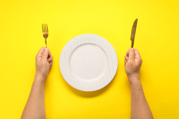 Man with fork, knife and empty plate at yellow table, top view