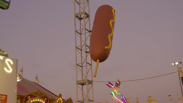 This video shows a giant corndog statue at a state fair in evening lighting.