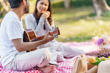 In love couple enjoying picnic time playing guitar in park outdoors Picnic. happy couple relaxing together with picnic Basket