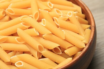 Raw penne pasta in bowl on table, closeup