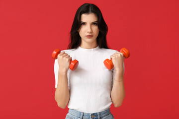 Young woman exercising with dumbbells on red background. Feminism concept