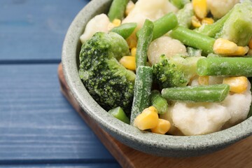 Mix of different frozen vegetables in bowl on blue wooden table, closeup. Space for text