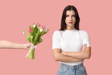 Confident young woman with crossed arms ignoring bouquet of flowers on pink background. Feminism...
