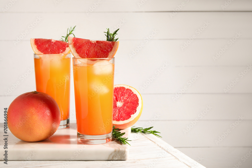 Canvas Prints Tasty grapefruit drink with ice in glasses, rosemary and fresh fruits on light wooden table. Space for text