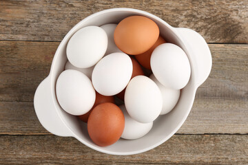 Unpeeled boiled eggs in saucepan on wooden table, top view