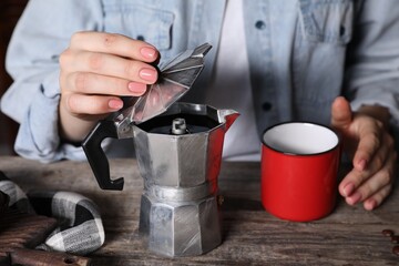 Fototapeta na wymiar Brewing coffee. Woman with moka pot and cup at wooden table, closeup